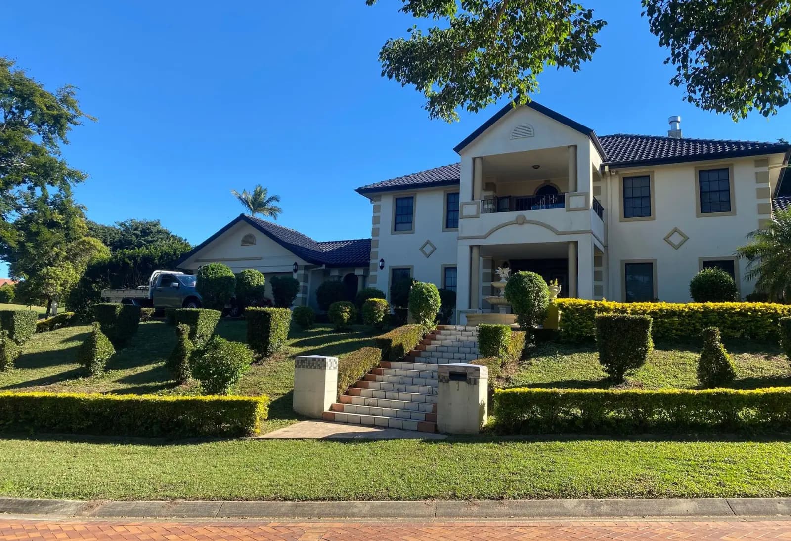 A maintained Brisbane front yard with clipped hedges, green lawn and a Plus One work ute